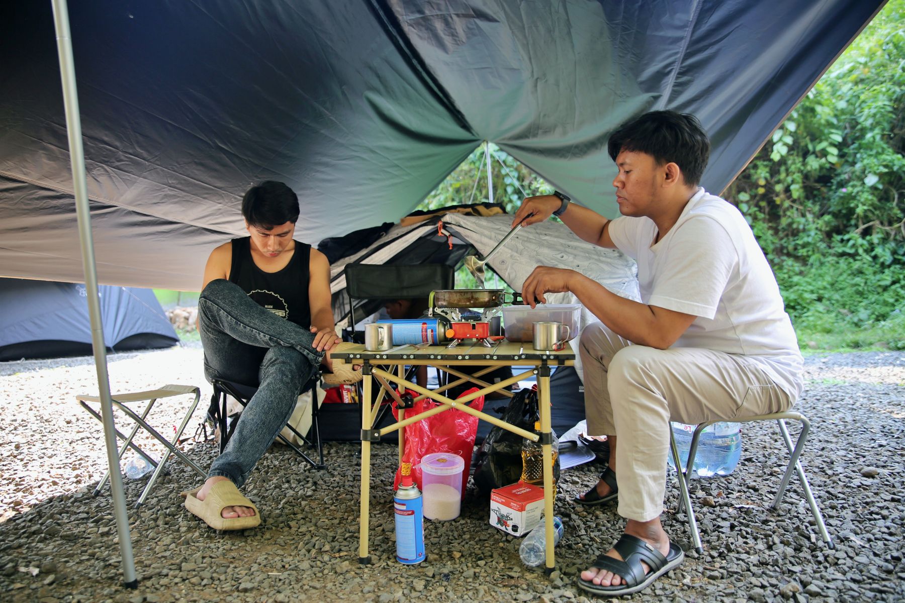 Campers preparing food under a tarp next to their tent
