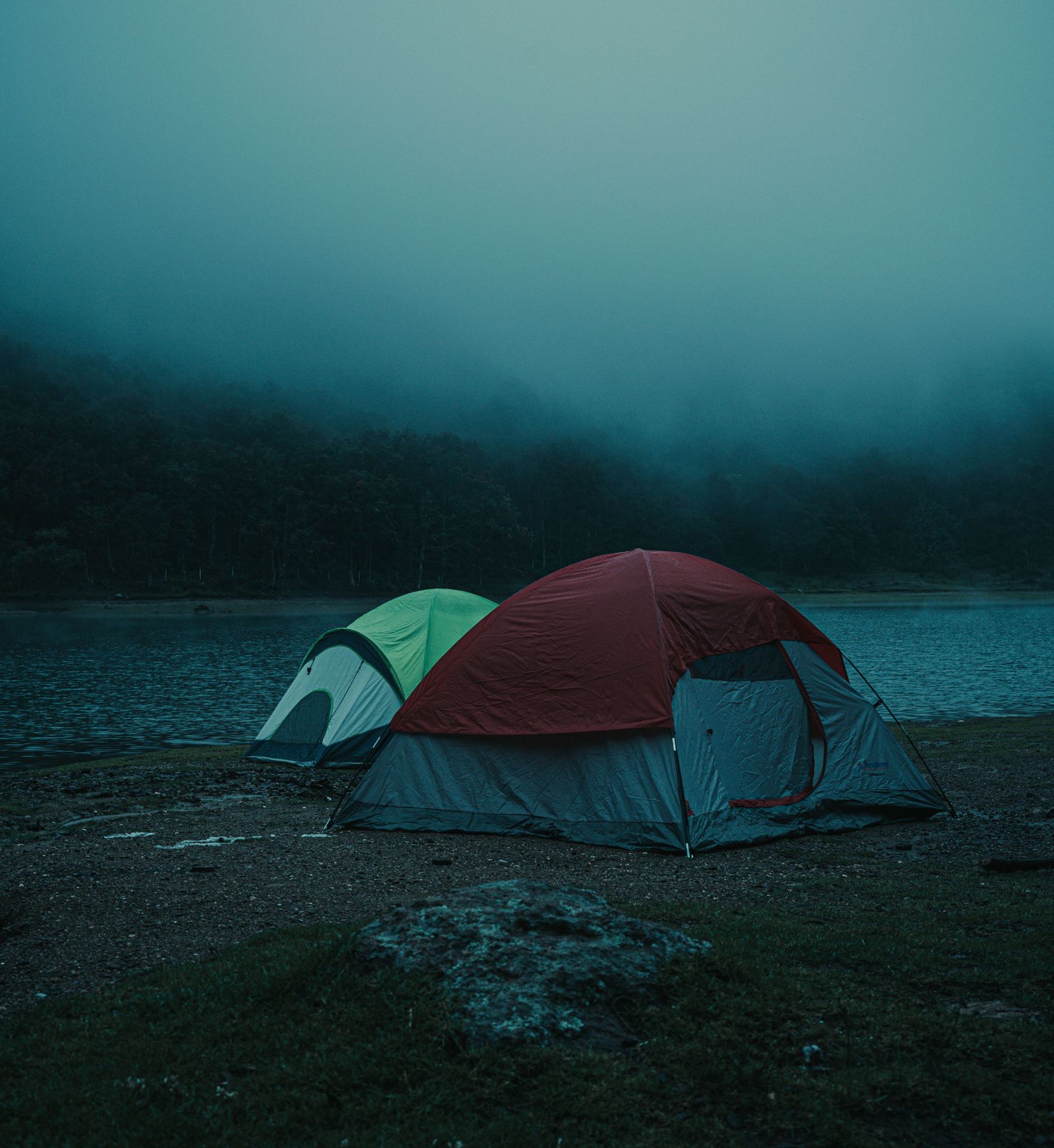 Two dome tents on a lakeshore in morning fog