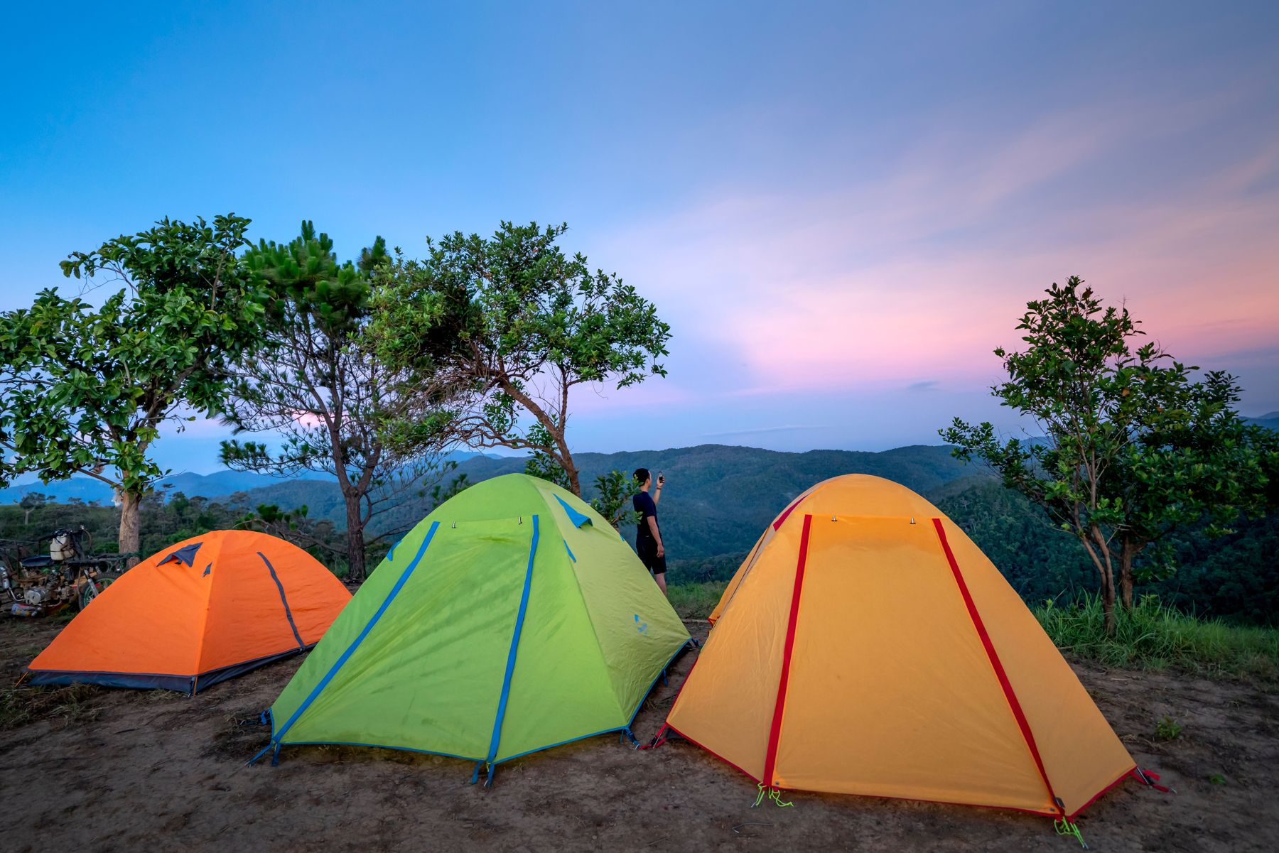 Camper photographing the view beside three dome tents on a mountain ridge